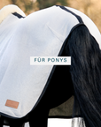 Black-and-white pony from behind wearing a light-coloured organic cotton cooler rug with lambskin trim, for ponies