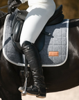 Mantilla de doma gris con ribete blanco bajo la silla de un caballo oscuro