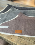 Two folded wool rugs in grey and taupe with cream binding