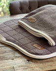 Sottosella trapuntato color tortora con bordo color crema e patch in pelle CHVX*N accanto a coperta antisudore piegata