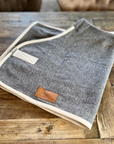 Grey-brown wool rug with cream binding, folded on wood