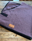 Lilac wool rug with black binding and buckle, folded on wood