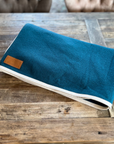Petrol blue wool rug with cream binding, folded on wood