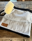 Light grey wool rug with lambskin roll and black binding, folded on wood