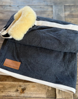 Dark grey wool rug with lambskin roll and cream binding, folded on wood