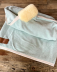 Mint wool rug with lambskin roll and rosé binding, folded on wood