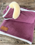 Berry wool rug with lambskin roll and white binding, folded on wood