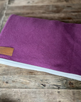Plum wool rug with white binding, folded on wood