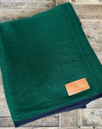 Fir green wool rug with dark binding, folded on wood