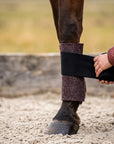Hand wickelt eine schwarze Bandage über eine bordeauxrote Bandagierunterlage aus Merinowolle